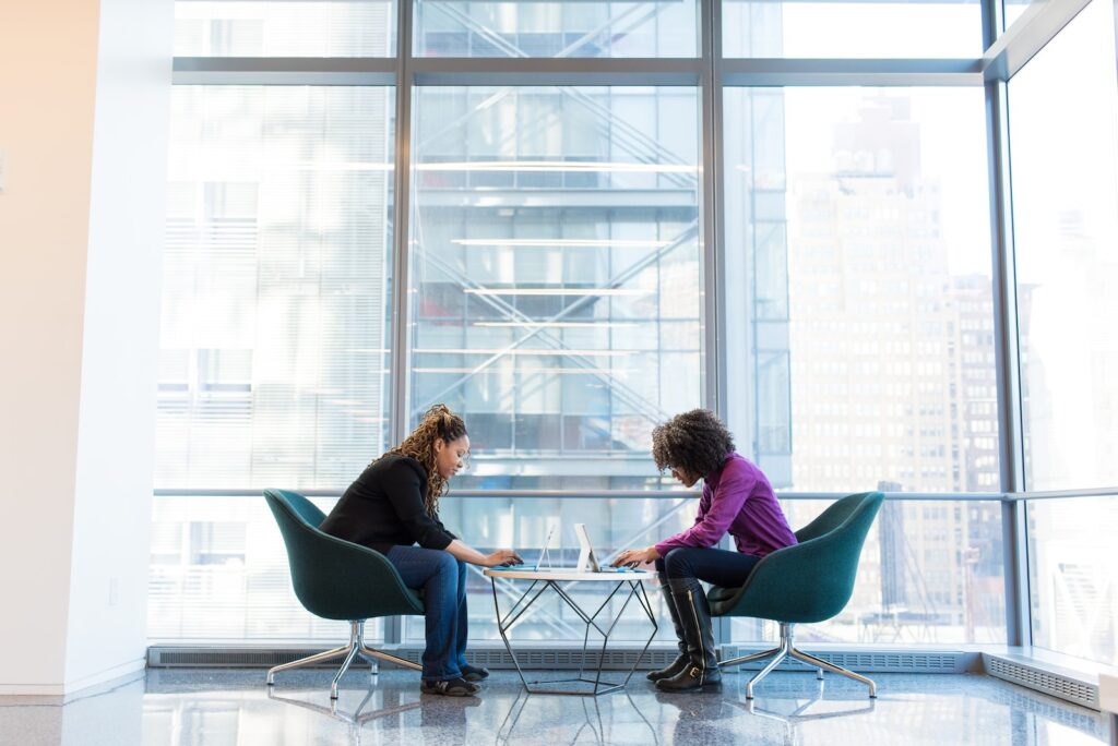 two women sits of padded chairs while using laptop computers - How to Start a Business