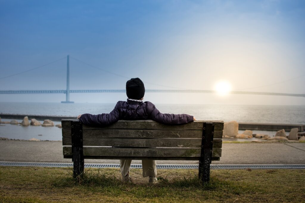 person sitting on bench facing suspension bridge - productivity tips