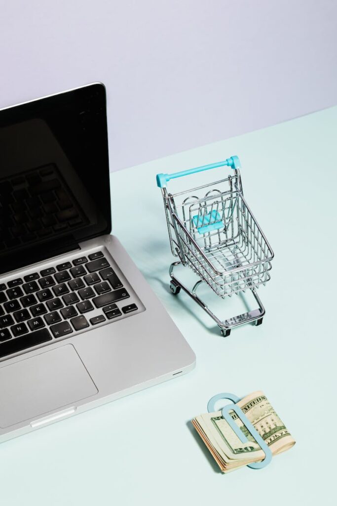 A Macbook Beside a Miniature Shopping Cart and Clipped Money - How to Start an eBay Business