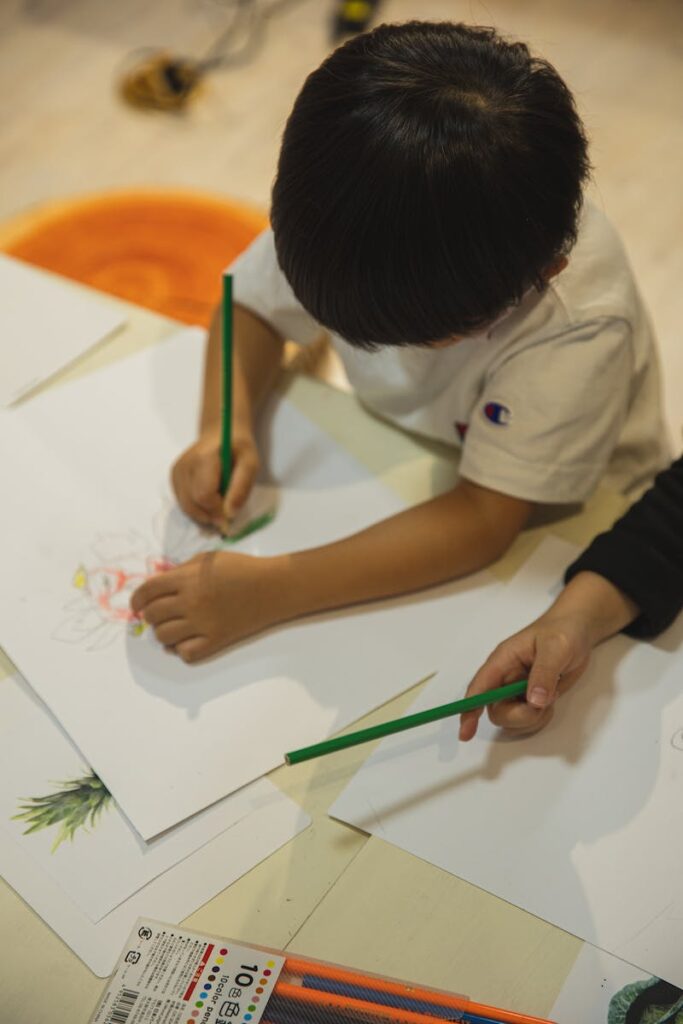 children's drawing classes - High angle of crop anonymous ethnic children drawing on paper sheet with pencils during art class in kindergarten