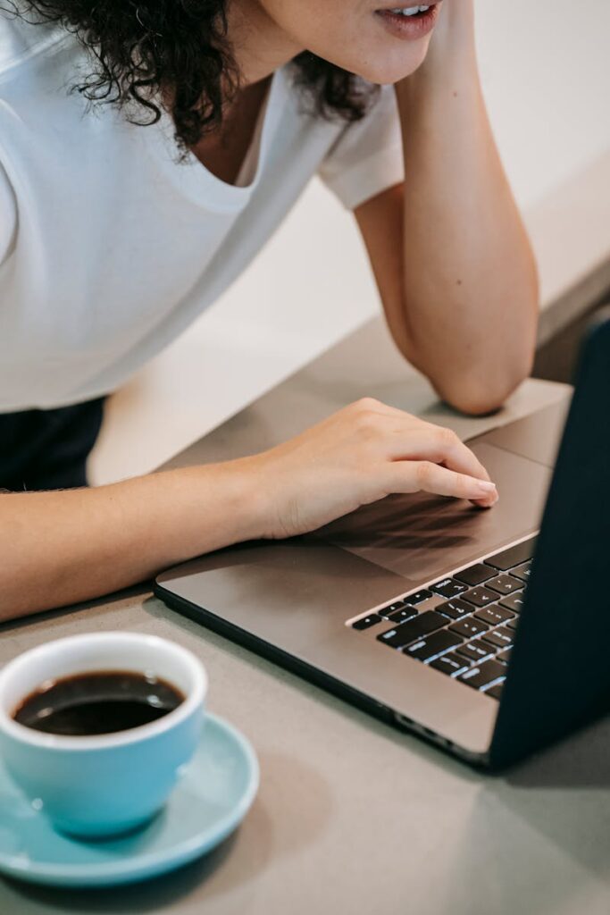 Woman working on laptop with coffee cup, Working remotely and maintaining team culture