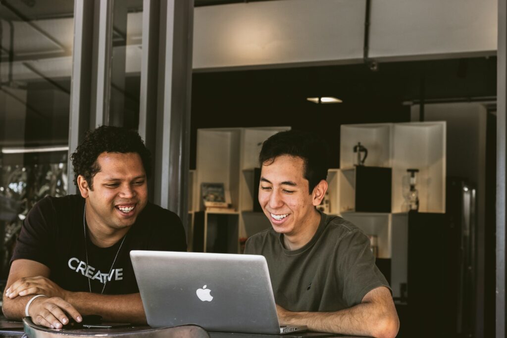 two smiling men looking at MacBook - starting a small business and embrace imperfections